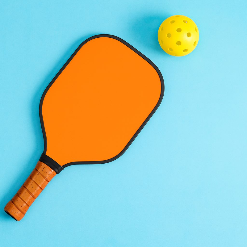Pala naranja y pelota perforada de pickleball sobre fondo azul